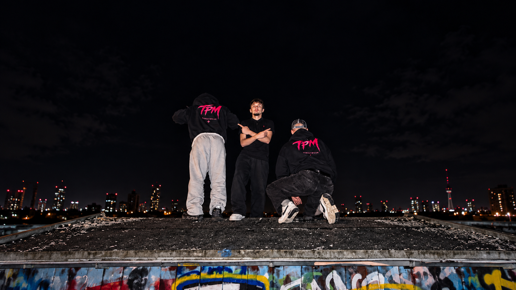 TPM Streetwear bei Nacht: schwarze Hoodies mit pinkem Rückenprint